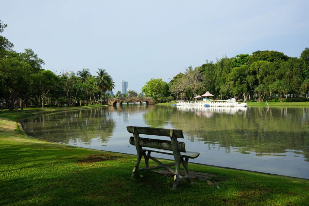 morning view of a bench by Lumpini Park lake with Bangkok skyline