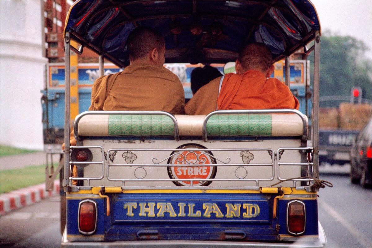 Two monks riding in a tuk-tuk in Bangkok, showing an everyday street scene and common short-distance transport