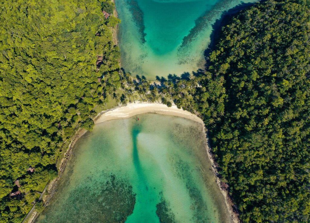 Aerial view of a serene Koh Chang bay with turquoise waters, lush greenery, and a sandy shoreline under a clear sky.
