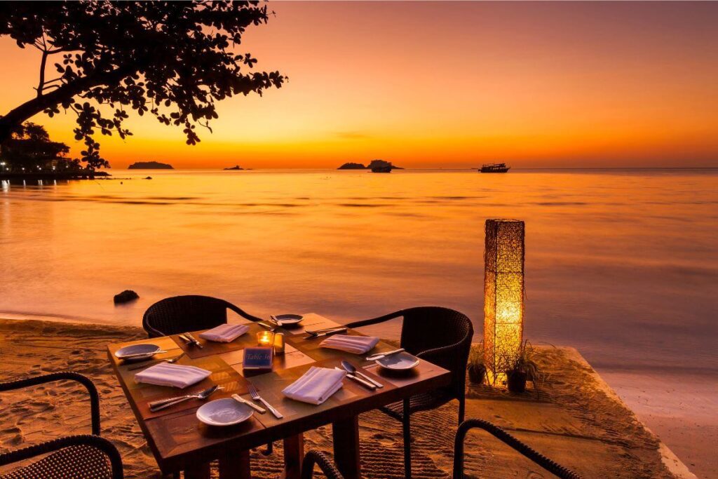 Romantic candlelit dinner on Koh Chang beach at sunset, with a table set for two, glowing candles, and the ocean in the background.