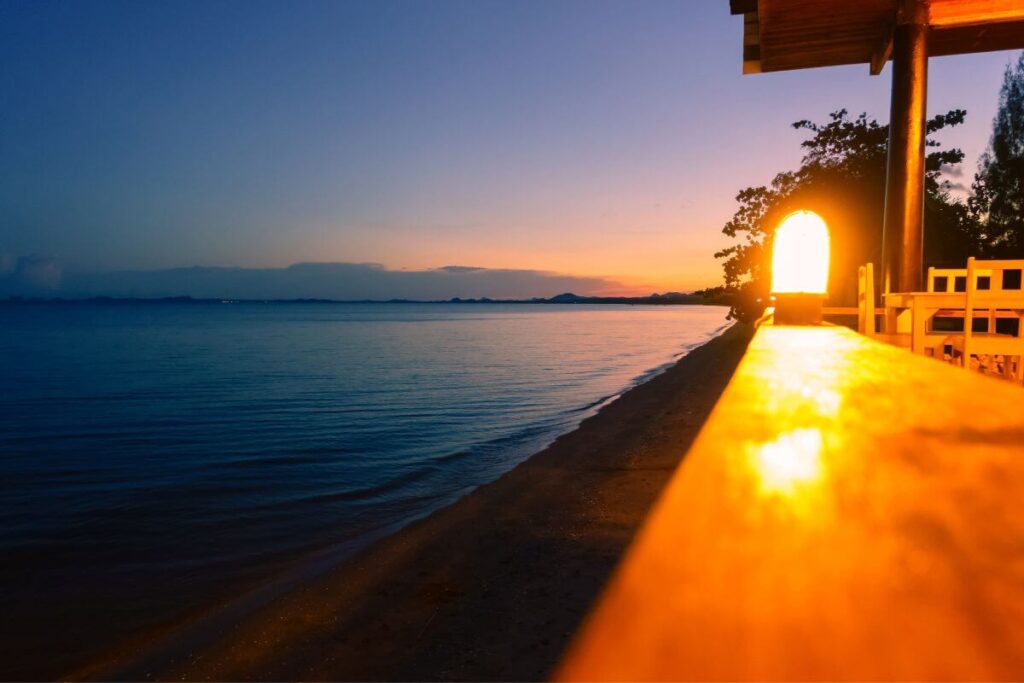 Sunset view from a beachside restaurant in Koh Chang, with tables set against a golden sky and calm ocean waves.