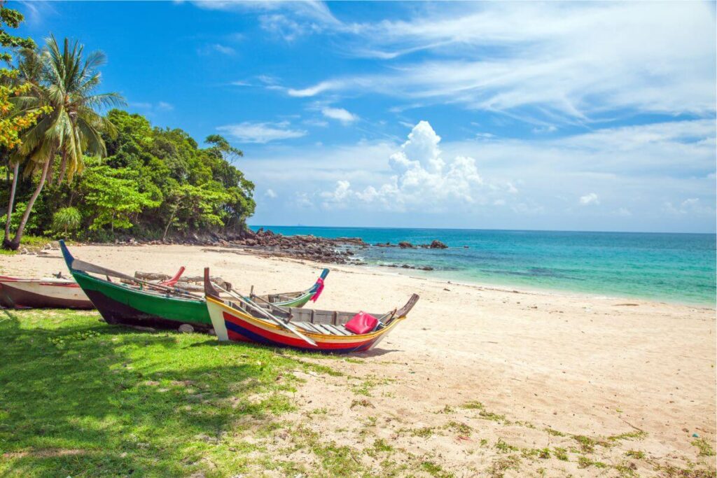 Small fishing boats line Koh Lanta’s beach shore under clear blue skies, with calm turquoise waters in the background.