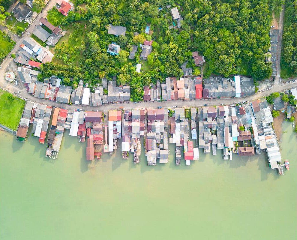 Aerial view of Koh Lanta’s Old Town next to the beach, with colorful buildings, sandy shores, and turquoise waters under a clear sky.