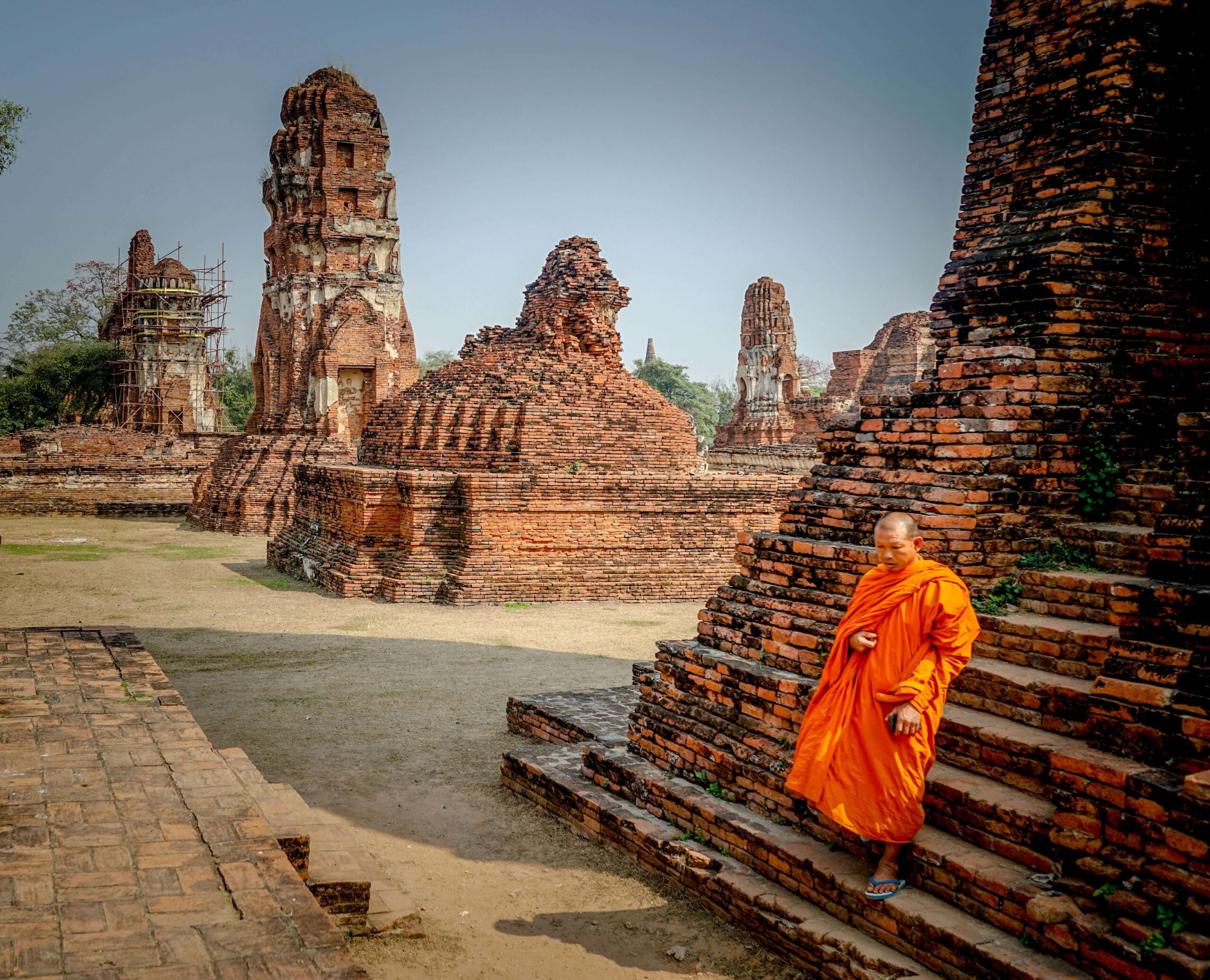 Monk in orange robes walking through ancient temple ruins in Ayutthaya