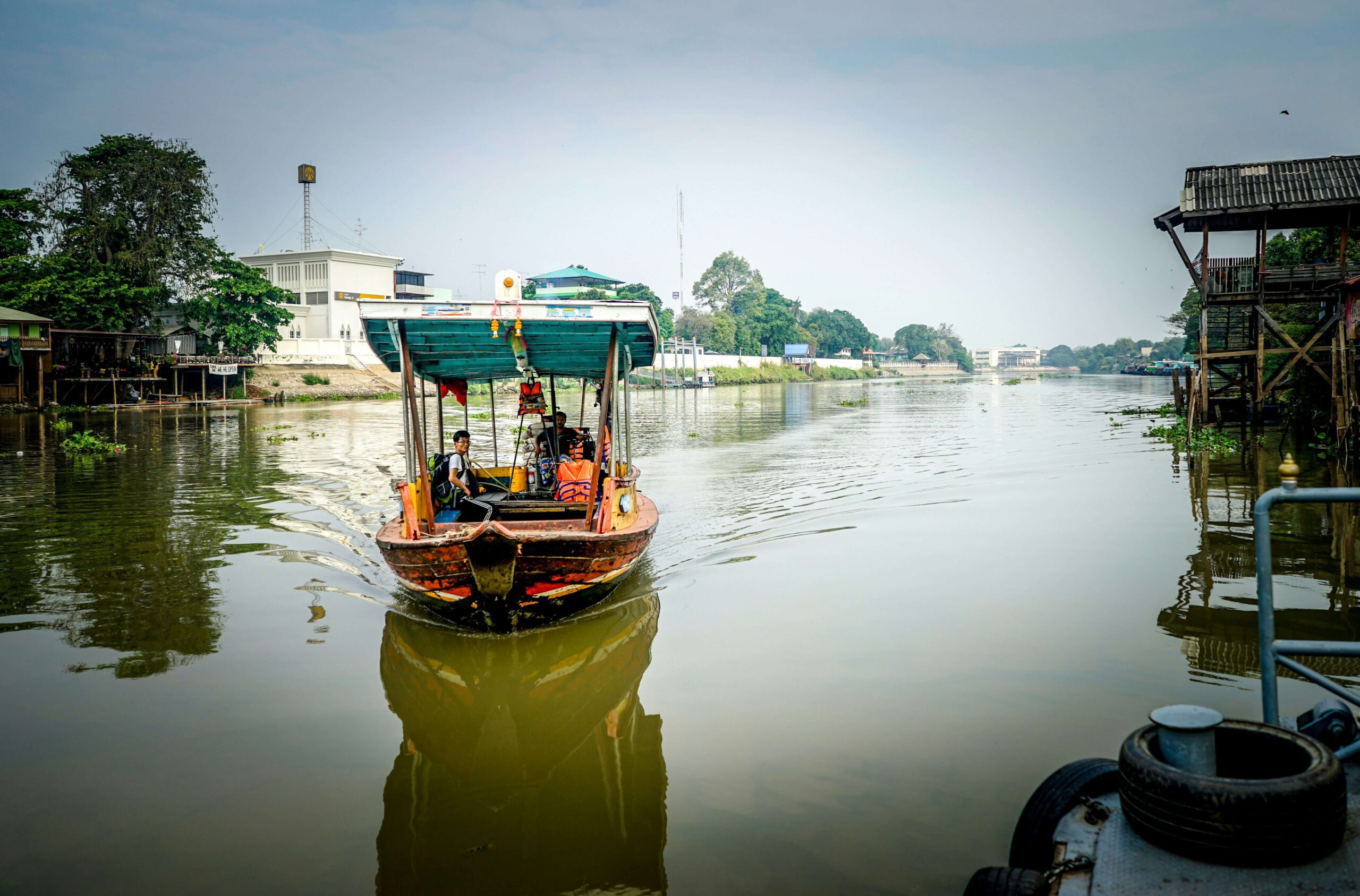 Private wooden boat passing ancient temple spires along the Chao Phraya River in Ayutthaya