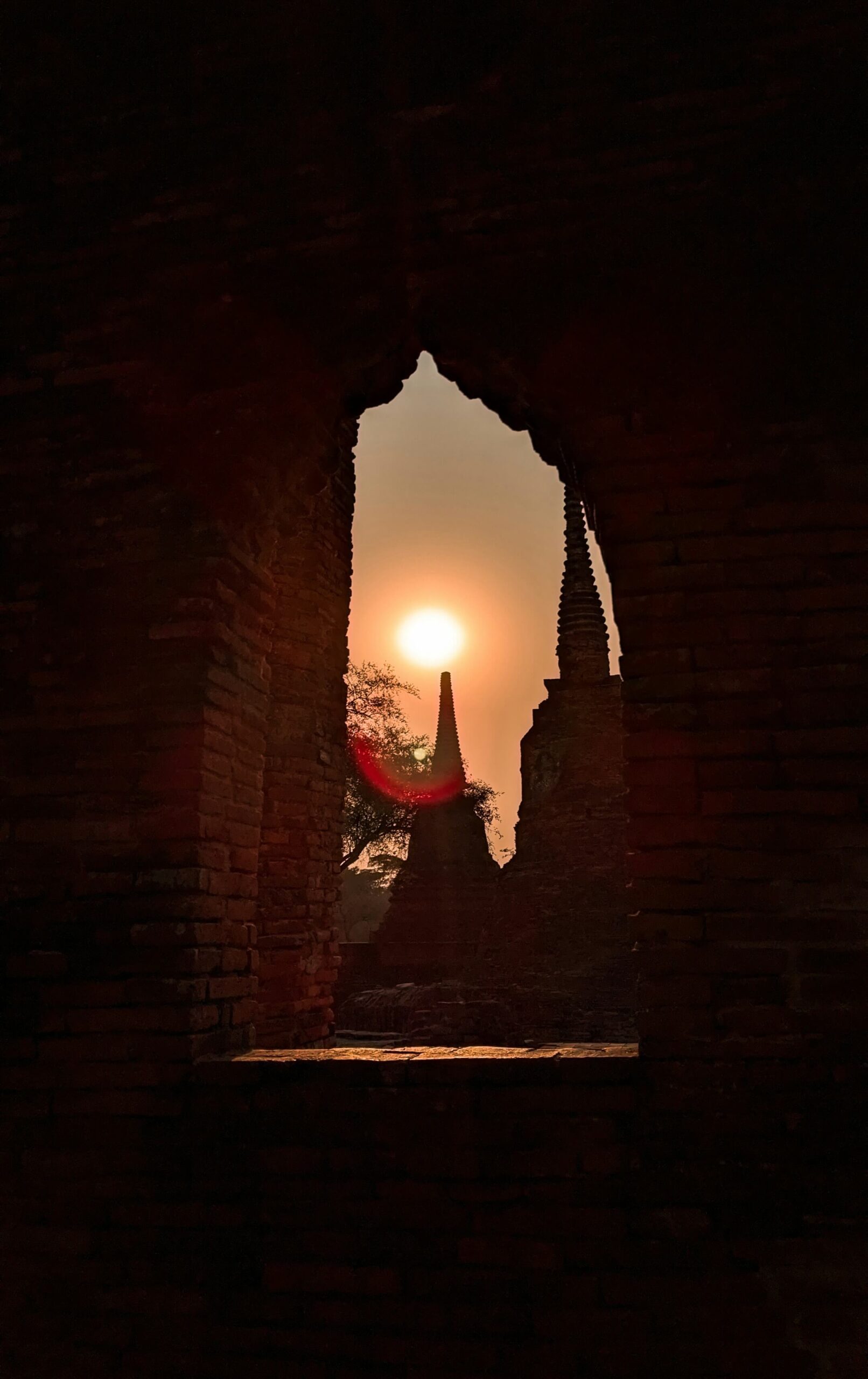 Golden hour sunlight illuminating the ruins of an Ayutthaya temple as seen from a stone walkway during a day trip