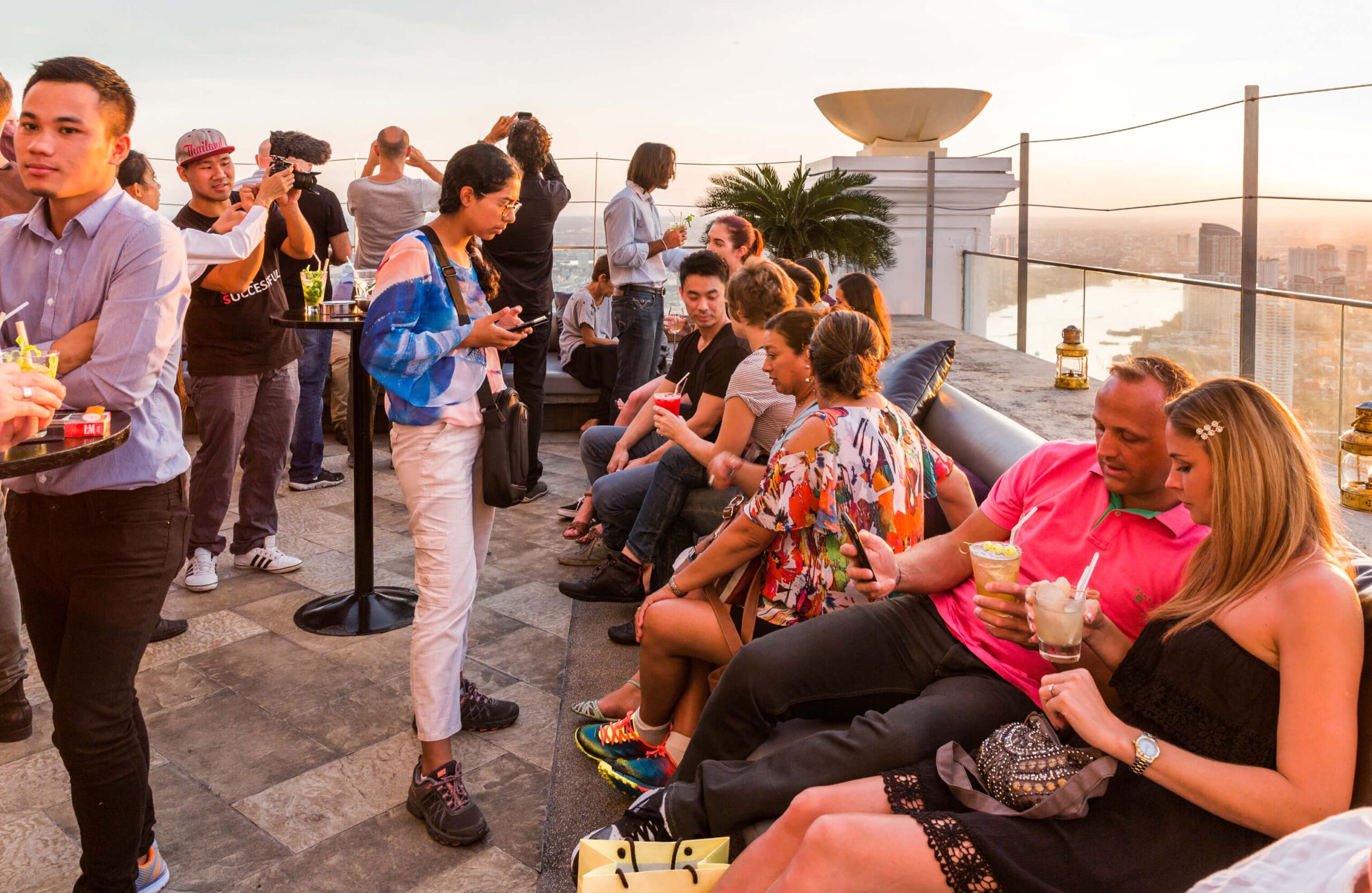 Rooftop bar view in Bangkok at sunset with a small crowd and skyline in the distance, showing an elevated city perspective in 2026