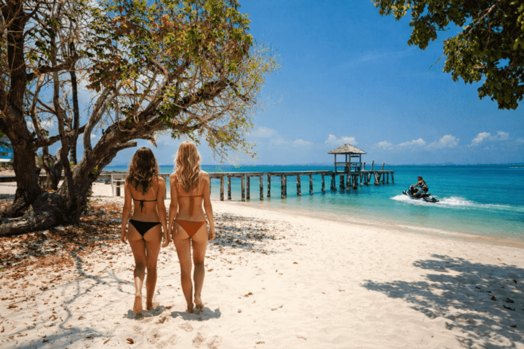 Two women walking along Koh Samet beach with a jet ski in the water, clear sea and tropical coastline near Bangkok